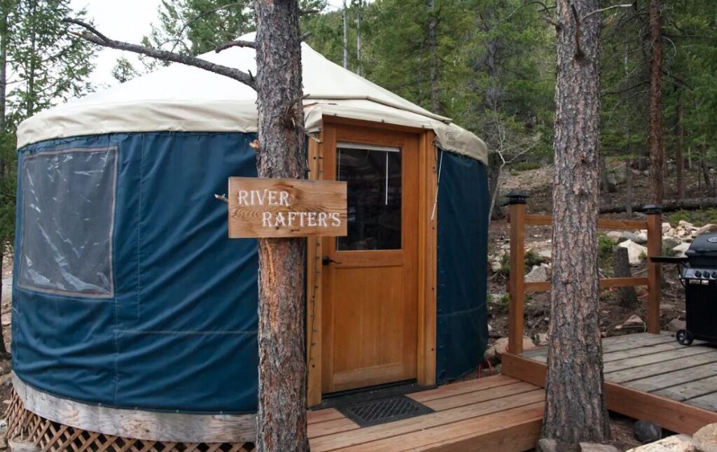 front view of a blue yurt set in the trees at Basecamp Lodging Co