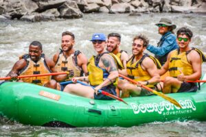 men in a green raft wearing life jackets and holding oars