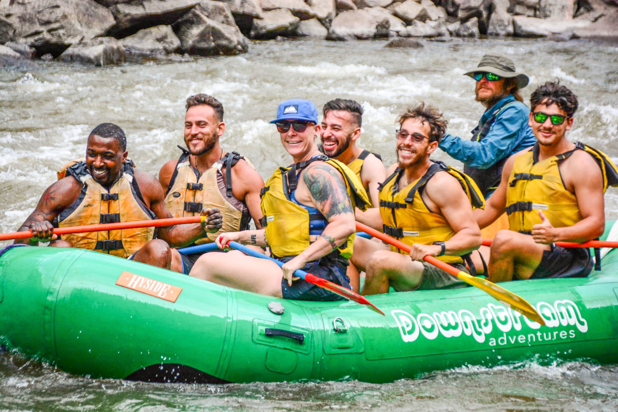 men in a green raft wearing life jackets and holding oars