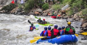 People rafting on Clear Creek in a raft that says Downstream on it with kayakers in front